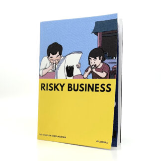 A thin comic sits on a white desk. The comic is titled RISKY BUSINESS and shows an illustration of child eating a sandwich next to their father who is reading the newspaper and also eating a sandwich at the same time.